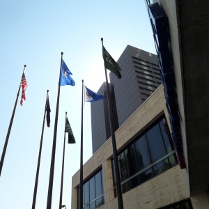 Flags at U.S. Bank Plaza, Minneapolis MN, Sep. 17, 2014. Hennepin Government Center in background. Four of the six flags appear to be corporate flags, along with U.S. and Minnesota. All flagpoles appear to be identical in height.